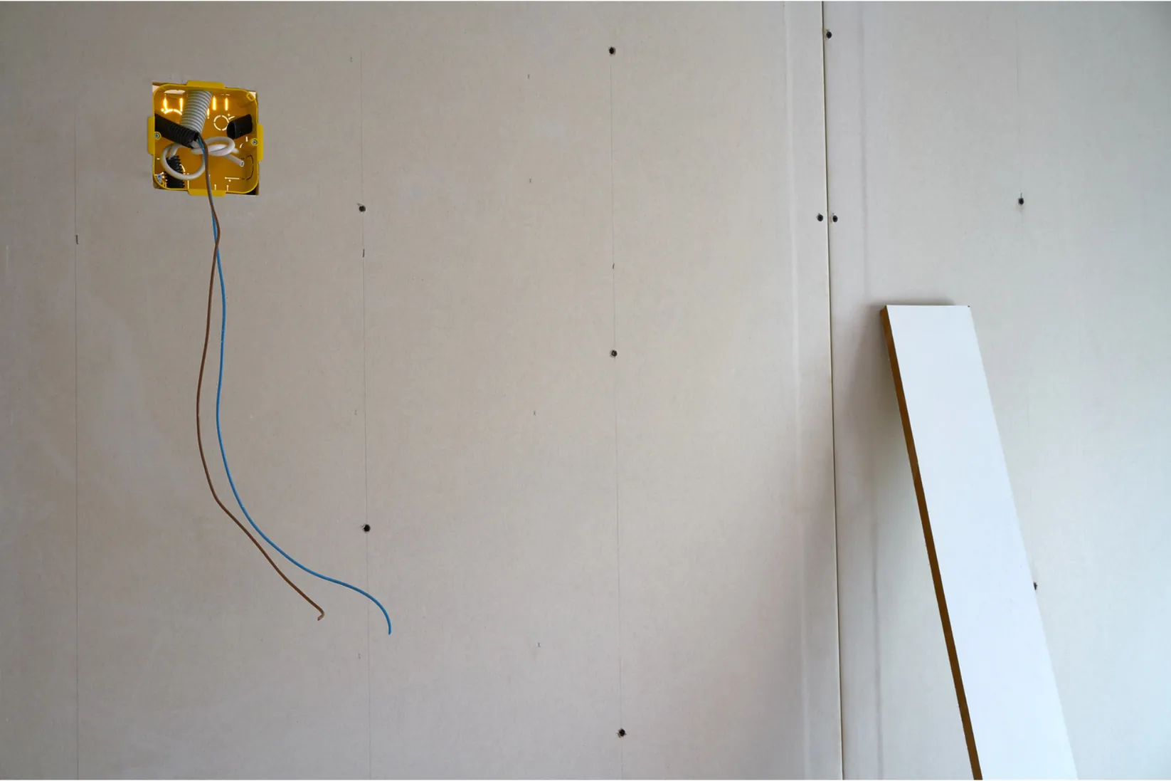 Gipskartonwand mit Schraubenreihen und offener Elektrodose